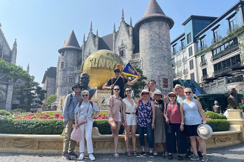 A group of people posing in front of a castle-like structure with a globe and a flag. 4