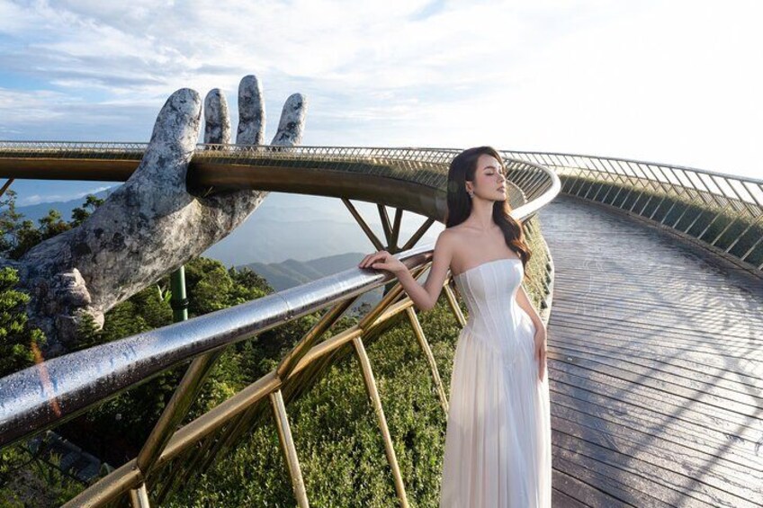 A person in a white dress standing on a wooden boardwalk with a large metal sculpture of a hand. 5