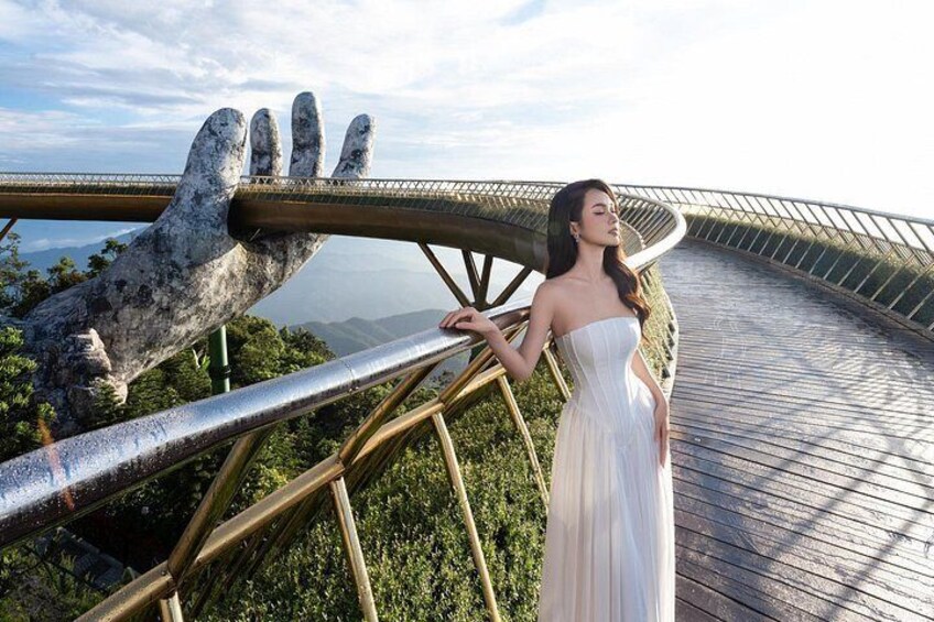 A woman in a white dress standing on a wooden bridge with a large hand sculpture. 3