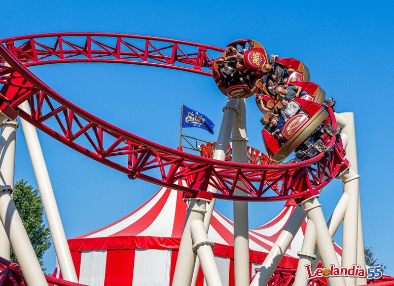 A roller coaster in motion with red tracks and a white and red striped canopy in the background. 3