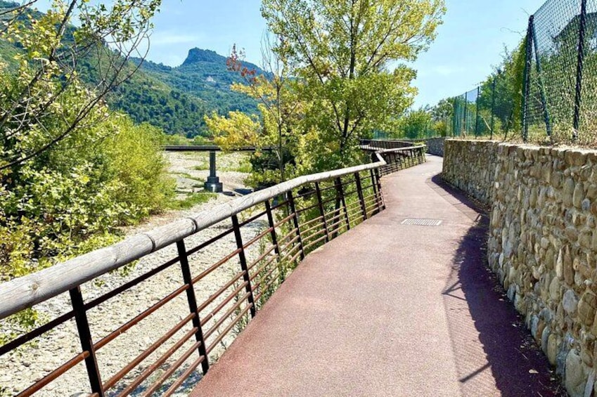 A paved walkway with metal railings, surrounded by greenery and a stone wall, leading towards a mountainous landscape. 4