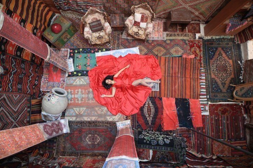 A person lying on a patterned carpet surrounded by various rugs and textiles. 4