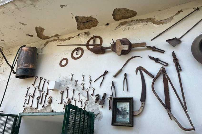 Una colección de herramientas y equipos antiguos, incluyendo martillos, cinceles y un balde, exhibida frente a una pared desconchada y un cuadro enmarcado. 5
