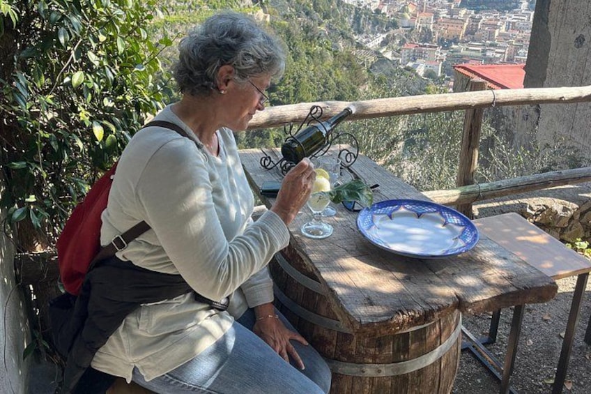 Una persona sentada a una mesa de madera con una botella de vino y copas, con vistas a un paisaje urbano. 4