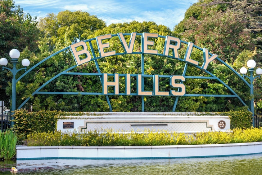 Segnaletica con la scritta 'BEVERLY HILLS', in primo piano una barca bianca e sullo sfondo vegetazione rigogliosa. 1