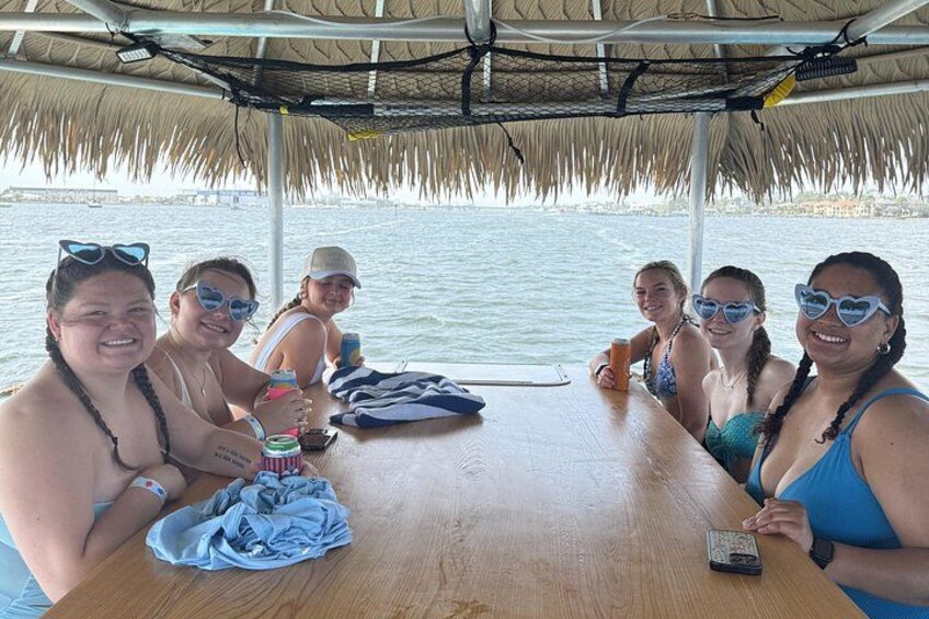 A group of people on a boat with a thatched roof, sitting at a wooden table with drinks and a smartphone. 4