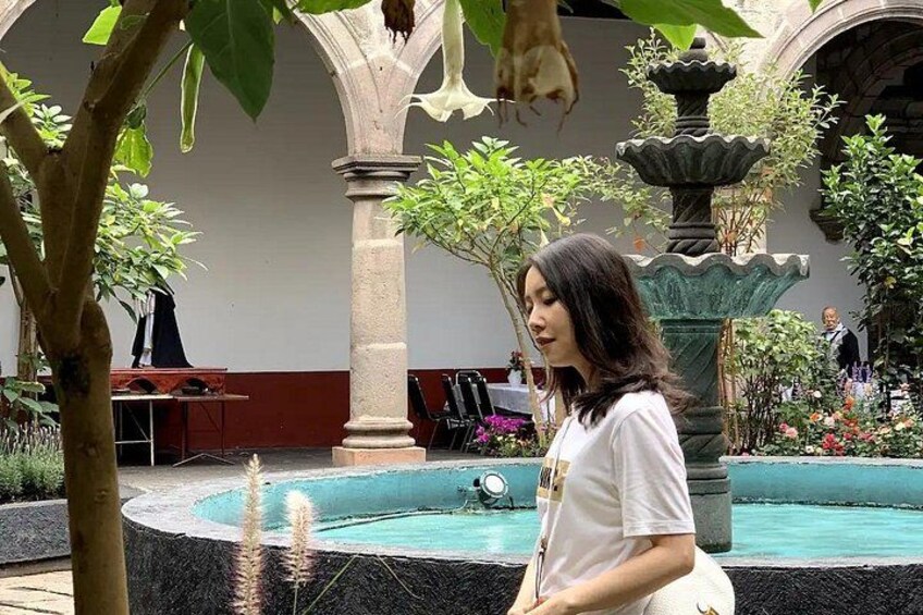 A woman standing in a courtyard with a fountain, surrounded by greenery and architectural columns. 5