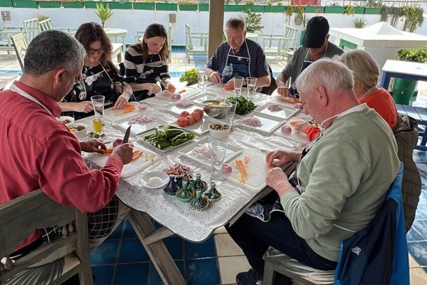 Un groupe de personnes est assis autour d’une table, à l’extérieur, et partage un repas et des boissons. 1
