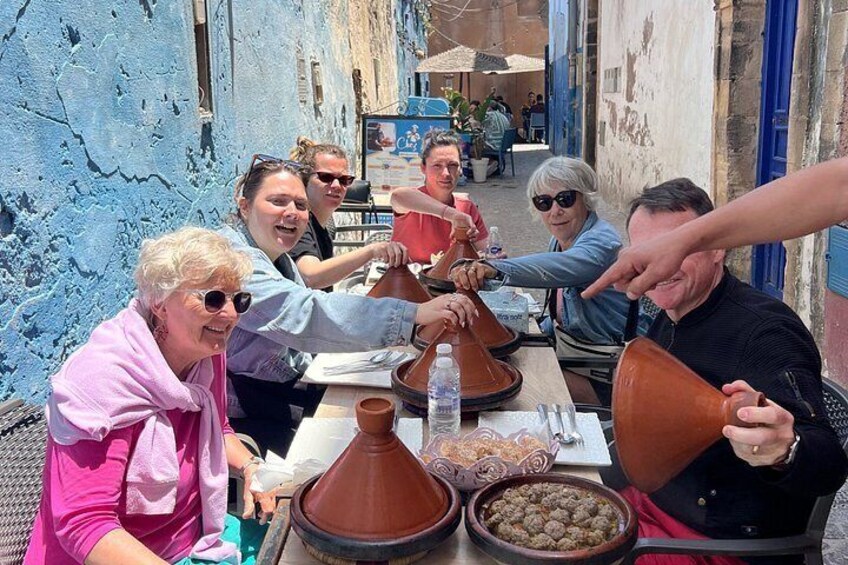 Un grupo de personas sentadas alrededor de una mesa con vasijas de barro tradicionales y un plato de comida. 2