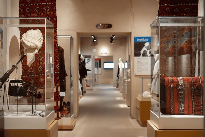 A museum corridor with glass display cases containing traditional textiles and artifacts. 2