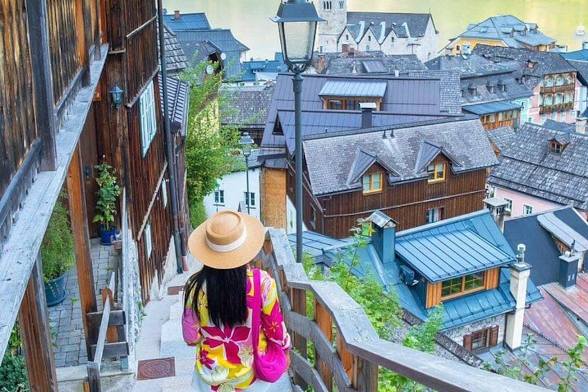 Eine Person geht eine Holztreppe in einem traditionellen Dorf mit Holzhäusern und einem Gebäude mit blauem Dach hinunter. 3