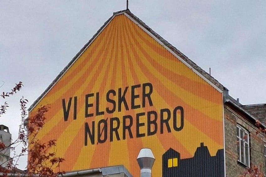 Un edificio con un mural que presenta el texto 'VI ELSKER NORREBRO' y una silueta de un paisaje urbano. 1
