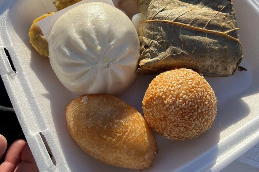 Ett fat med en ångkokt bulle, en risbulle inlindad i ett blad, en bulle med sesamfrön och en friterad degbit. 2