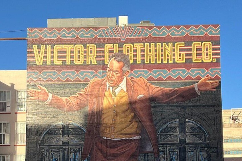 En väggmålning som föreställer en man i kostym med utsträckta armar, och texten ”VICTOR CLOTHING CO.” står på en byggnad. 3