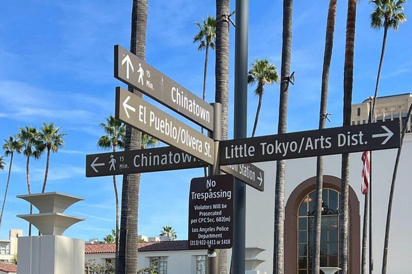 En vägskylt med flera pilar som visar vägen till olika destinationer, till exempel Chinatown, El Pueblo/Olvera St. och Little Tokyo/konstkvarteren. 1