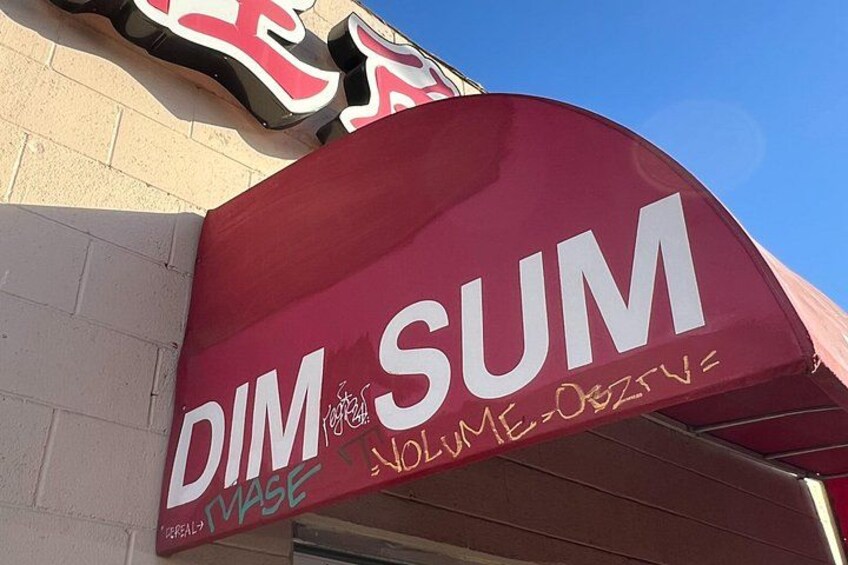 En byggnad med ett rött markis där orden ”DIM SUM” och ”VASE” är skrivna med vita bokstäver. 4
