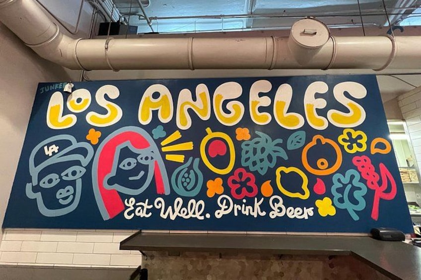En färgstark väggmålning med texten ”Los Angeles – ät gott, drick öl” och olika illustrationer av mat och dryck. 2