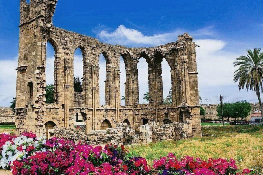 An ancient stone structure with multiple arches and columns, surrounded by vibrant flowers. 2