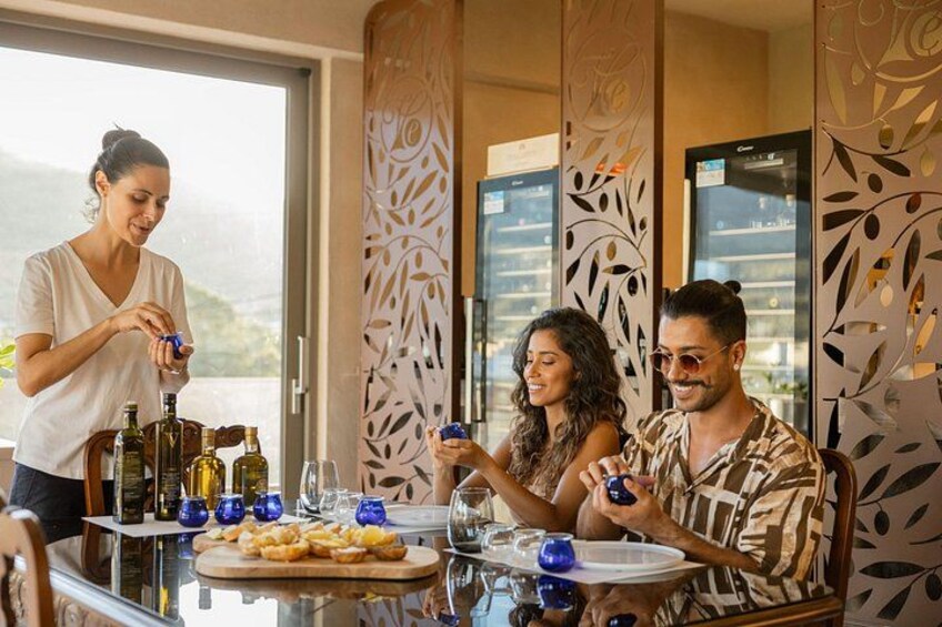 A group of people at a table with wine bottles and glasses, a plate of food, and a decorative wall. 1