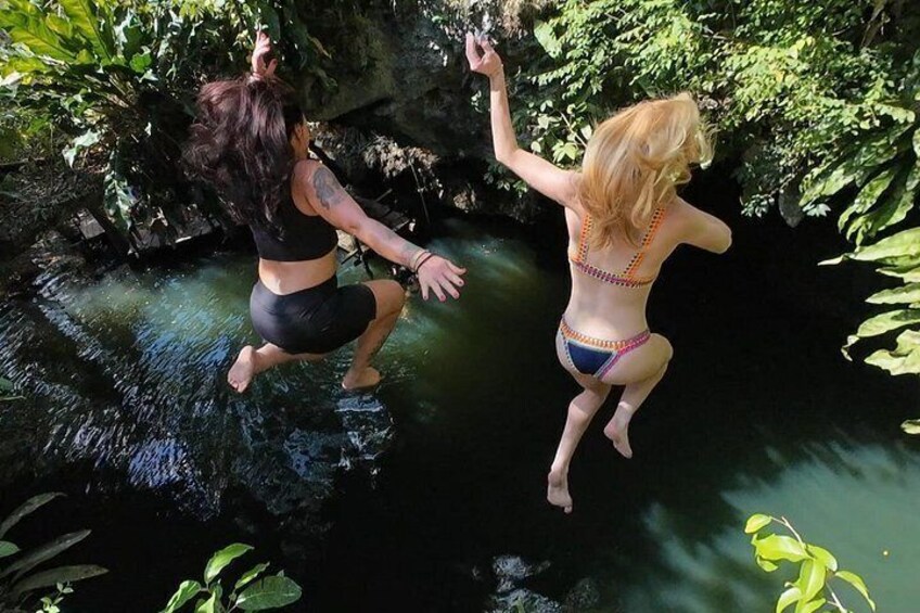 Two people jumping into a natural pool surrounded by greenery. 2