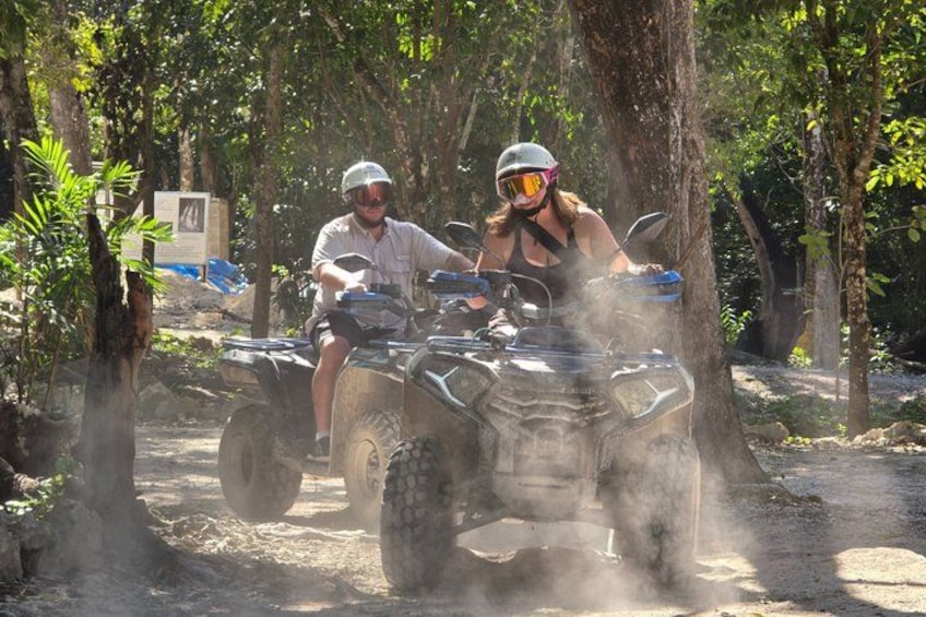 Two people riding atv's on a dirt path surrounded by trees. 3