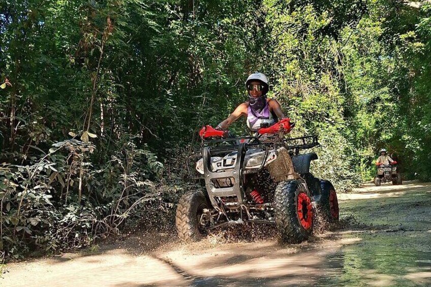 A person riding an ATV on a dirt road surrounded by dense foliage. 3