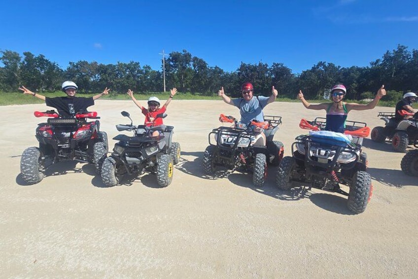 Four people on ATVs with their arms raised, on a clear day. 2