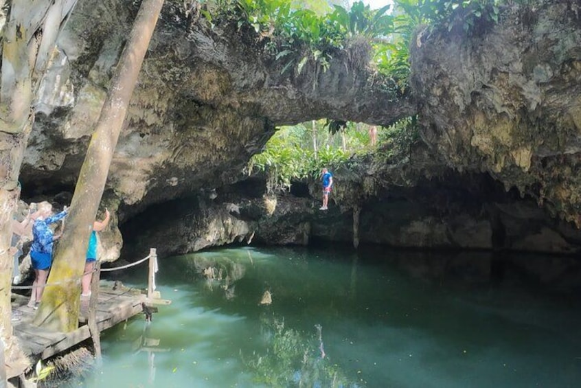 A cave with a water pool, a wooden walkway, and a person standing on a rock. 1