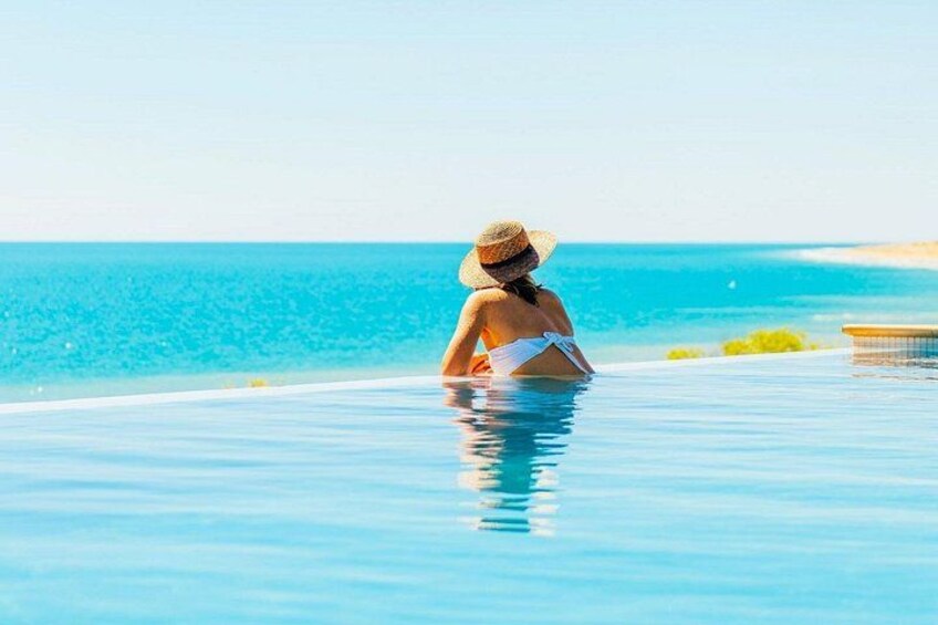 Une personne assise dans une piscine, avec une plage et l’océan en arrière-plan. 1