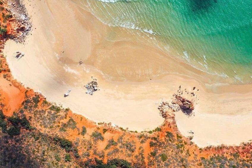 Vue aérienne d’une plage aux eaux turquoise et limpides, bordée d’un rivage sablonneux et d’une végétation clairsemée. 3