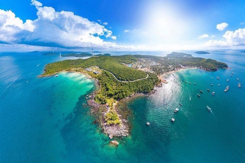 Luchtbeeld van een kusteiland met helder turquoise water, een dichtbegroeid bosgebied en verschillende boten afgemeerd nabij de kust. 5