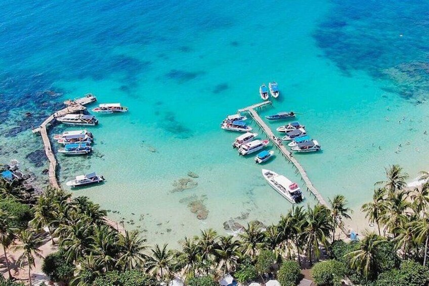 Een kustgebied met boten afgemeerd aan steigers, helder turquoise water en palmbomen. 3