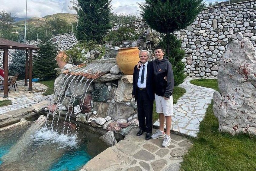 A man and a woman standing by a stone waterfall pool with a stone wall and a pergola in the background. 2