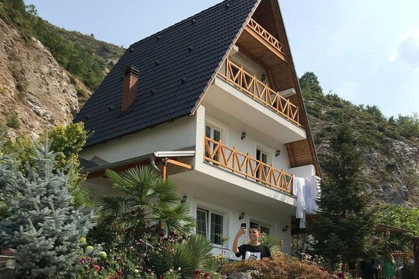 A two-story house with a steeply pitched roof, wooden balcony railings, and a garden with various plants and flowers. 3