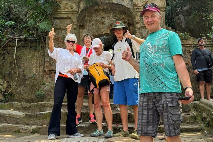 A group of people standing in an outdoor setting with stone structures and greenery in the background. 5