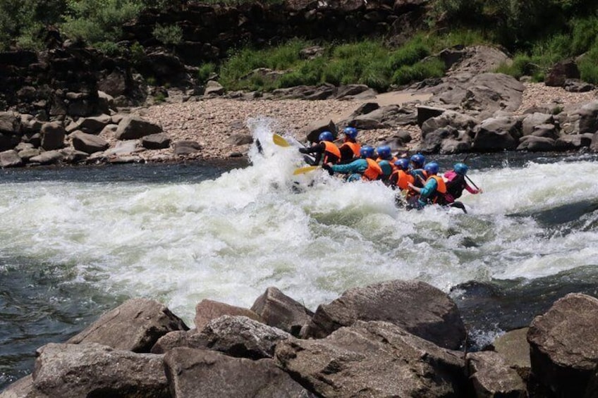 A group of people rafting on a river with rapids, surrounded by rocks and greenery. 1