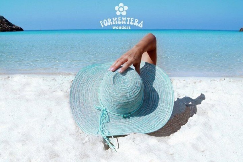 A turquoise straw hat on a sandy beach with clear blue water and a rocky outcrop in the distance. 2