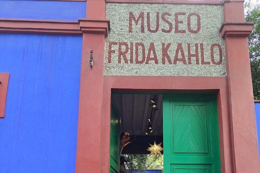A building with a sign reading 'MUSEO FRIDA KAHLO' and a green door. 1