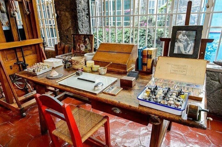 Un escritorio de madera con material de arte, un tablero de ajedrez y un cuadro enmarcado. 3