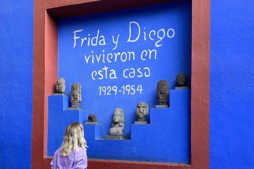 Una pared azul con una placa que dice 'Frida y Diego vivieron en esta casa 1929-1954' y varias esculturas de piedra. 5