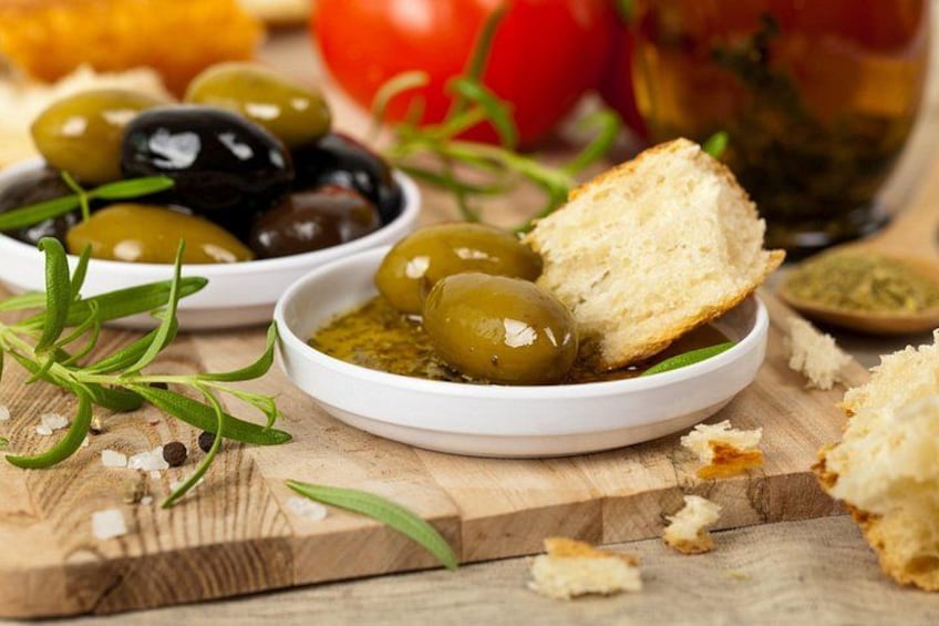 A wooden cutting board with olives, bread, and herbs. 2