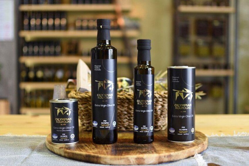 A selection of extra virgin olive oil bottles and cans on a wooden board, with a blurred background of shelves. 3