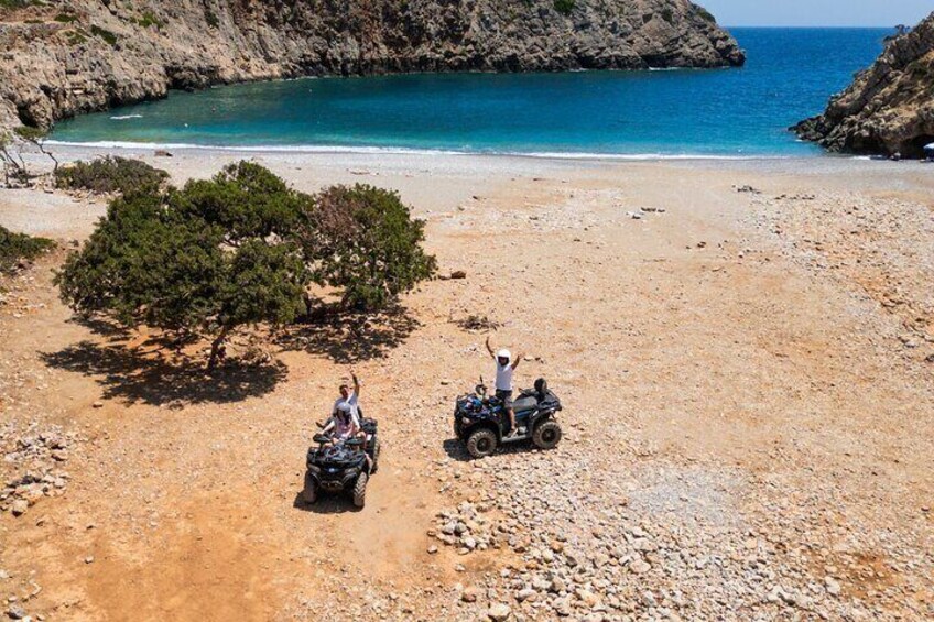Dos personas en cuatrimotos sobre una playa rocosa, con un árbol y un acantilado rocoso al fondo. 4