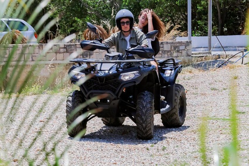 A person riding a quad bike on a gravel path with a stone wall and greenery in the background. 2
