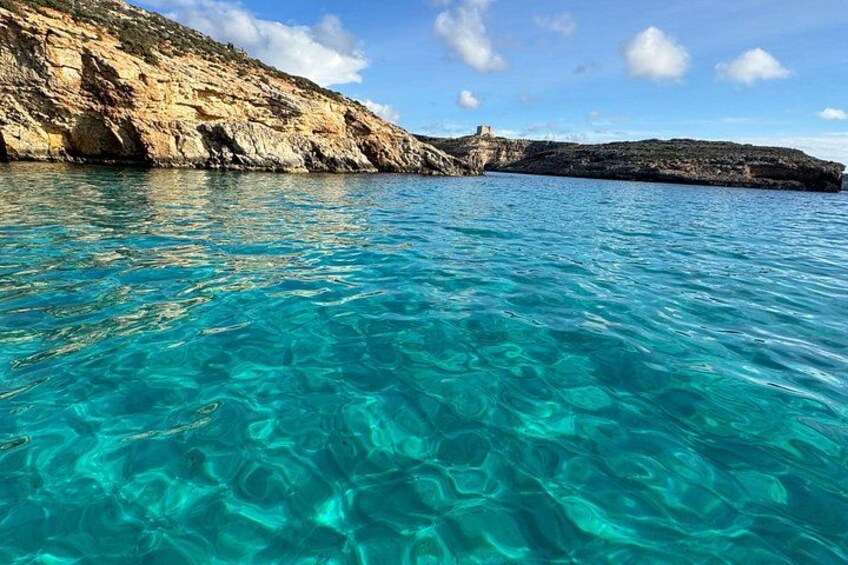 Clear turquoise water, rocky coastline, and a small building on a cliff. 2
