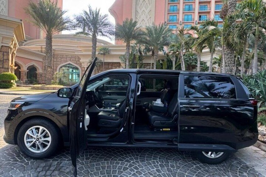 A black SUV parked on a cobblestone surface with open doors, palm trees, and a large building in the background. 3