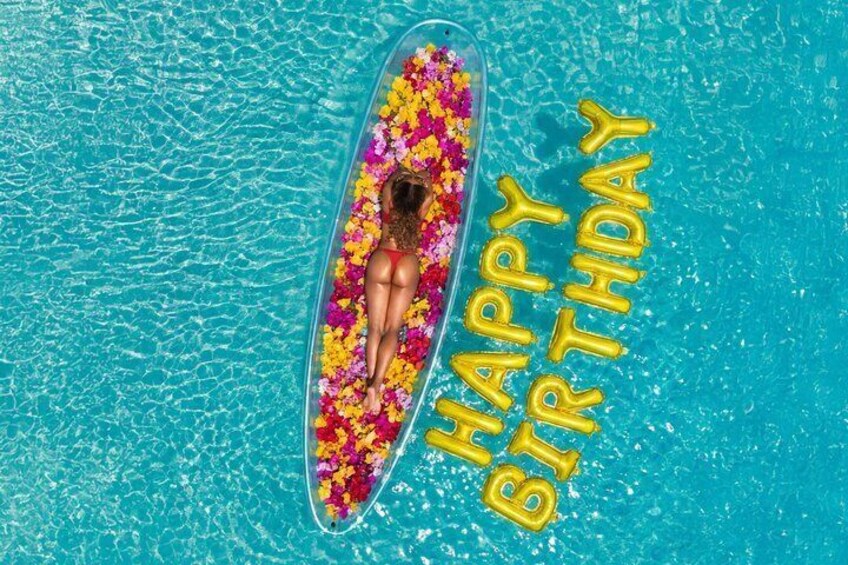 A person floating on a clear water surface with colorful flowers and 'HAPPY BIRTHDAY' balloons. 3