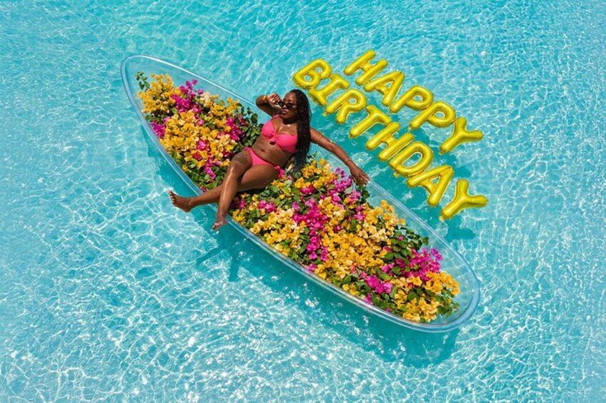 A person floating on a raft in a pool with colorful flowers and the text 'HAPPY BIRTHDAY'. 2
