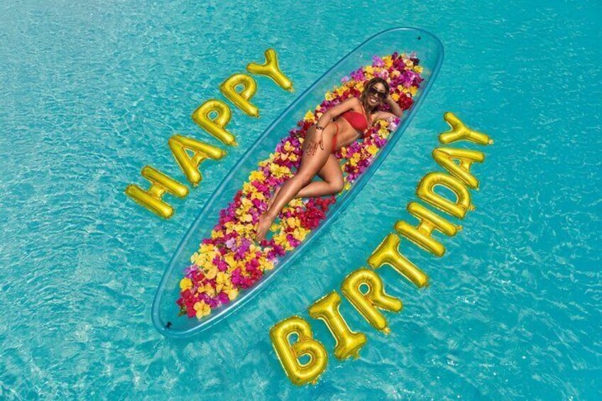 A person floating on a clear inflatable in a pool surrounded by yellow balloons spelling 'HAPPY BIRTHDAY.' 4