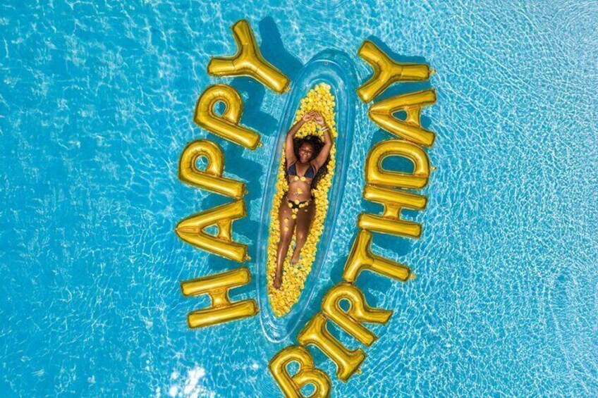 A person floating on an inflatable in a pool surrounded by golden balloons spelling 'HAPPY BIRTHDAY'. 5